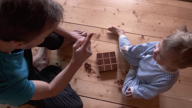Child and father playing board game at home. Son and dad play rock paper scissors, then tic tac toe. Parent spend time with kid while quarantine and self-isolation. View from above.