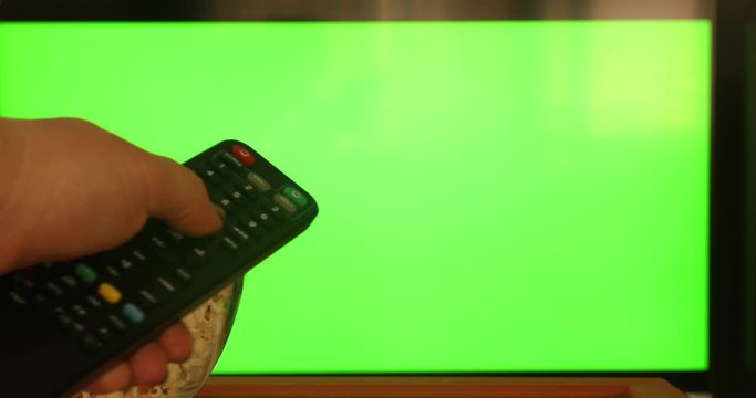 Female hand using a remote control to channels on flat green screen TV Watching television with snack