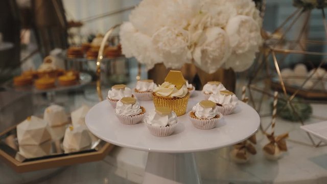 Delicious candy bar with cupcakes and mousse desserts in white color decorated with white peony bouquet, sweet table catering