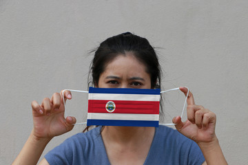 A woman with Costa Rica flag on hygienic mask in her hand and lifted up the front face on beige...