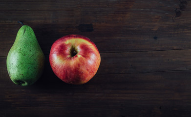 Top view of ripe organic fruits. Red apple and green pear on the old wooden table, dark tone, copy space for text.