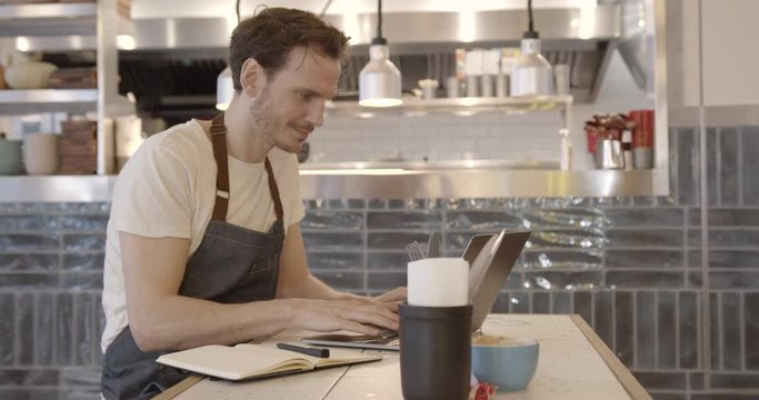 Chef in restaurant doing finance on laptop, small business, technology, entrepreneur