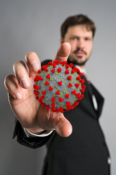 man with coronavirus model in his hands in front of grey background