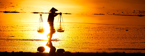 Salt and Silhoutte of salt farmer on salt field Hon Khoi, Nha Trang, Khanh Hoa, Vietnam.
