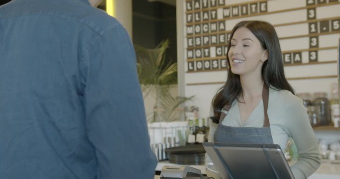 Female barista in cafe serving customer and receiving payment using smart phone