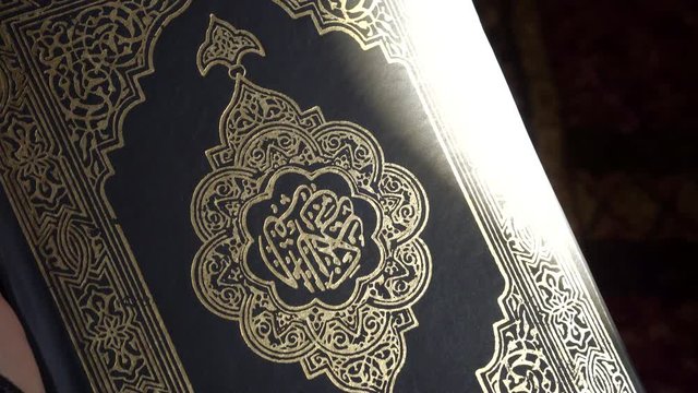 Sunlight hitting cover of Muslim Quran Islamic holy books shiny black and gold print