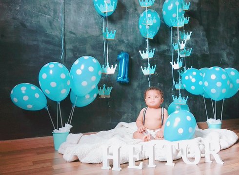 Baby Boy Sitting By Blue Balloons On Blanket At Home