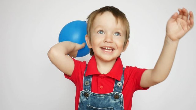 A happy little boy lifts up a blue balloon and throw it
