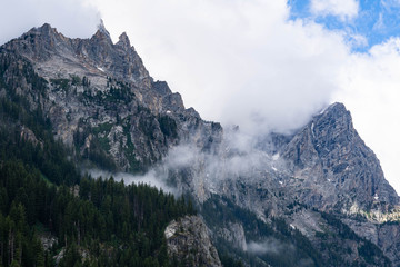 Grand mountains Grand Tetons in Wyoming. Mountain landscape with spring waters and mountain lakes. Blue sky. White clouds. Deep forest woods. 