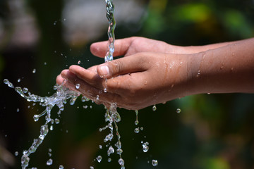 Water pouring in kid two hand on nature background. Hands with water splash.