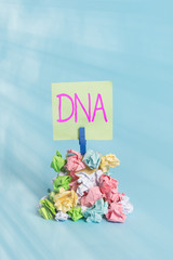 Handwriting text writing Dna. Conceptual photo a selfreplicating material wpresent in nearly all living organisms Reminder pile colored crumpled paper clothespin reminder blue background