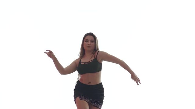 Medium long shot of young beautiful woman with long hair and a beautiful plump figure in a black top and a short black skirt dances belly dance, oriental dance on a white background,  isolated