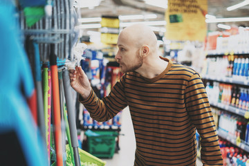 Adult bald bearded man shocked by the price in hardware department of supermarket