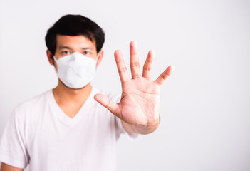 Closeup Asian handsome Man wearing surgical hygienic protective cloth face mask against coronavirus and raising hand stop sign, studio shot isolated white background, COVID-19 medical concept