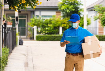 Asian young delivery man courier hold parcel post boxes he protective face mask service and walk looking for customer home location, under curfew pandemic coronavirus COVID-19