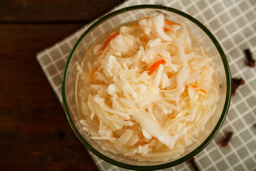 Plate with sauerkraut on a white towel and sprinkled spices on a wooden table.