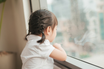 Back view at cute little girl looks out of the window