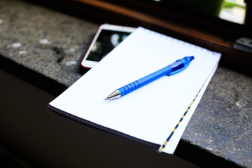 Close up of Dark blue pen, cell phone and white clear paper note on dark marble window sill....