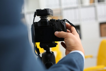 Male arms in suit mount camcorder to tripod making promo videoblog or photo session in office...