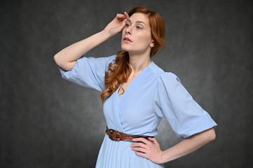 Girl Model posing in the studio on a gray background. Portrait of a pretty red-haired young woman in a blue blouse.