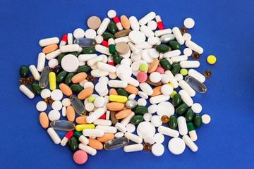 A pile of pills and capsules scattered on a blue background in different shapes, sizes and colors. Prevention and treatment during the period of the coronavirus pandemic. Top view.