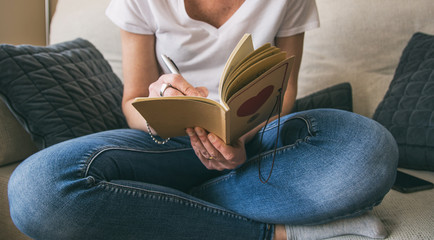 Unrecognizable woman taking notes sitting on the sofa at home