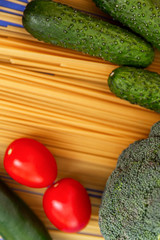 Fresh cucumbers, tomatoes and broccoli on sprinkled spaghetti. A healthy lifestyle and a Mediterranean diet. Delivery during the coronavirus pandemic. Blue background. Vertical.