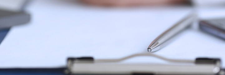 Silver pen lying on opened notebook sheet closeup in office with laptop pc on worktable. Inspector occupation for student examination or career strategy personal training course signature concept