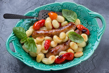 Sausage bake with potato gnocchi and bell peppers in a green serving tray, horizontal shot on a grey concrete background