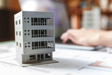 Close up of a house model standing over apartment plans in front of a laptop in a construction bureau.