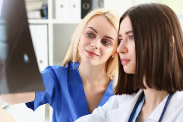 Fototapeta premium Group of beautiful female doctors hold in hand and look at xray photography to detect problem. Bone disease exam, medic assistance, cancer aid, healthy lifestyle, ill test, hospital practice concept