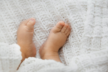 Top view of tiny baby girl feet on white blanket as a background, closeup of infant legs