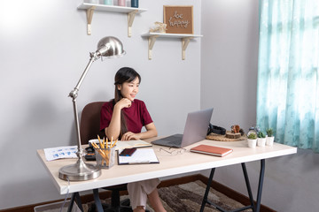 A young, beautiful relaxing business asian girl use a laptop working remotely from home on desk as a freelancer, quarantine for Coronavirus and smart working concept.