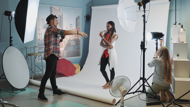 Backstage of the photo shoot: assistant adjusting the spotlight while photographer taking photos of pretty black model - Powered by Adobe