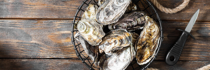 Lots of oysters in a black metal basket on a brown wooden table. Rustic style. French cuisine. Banner