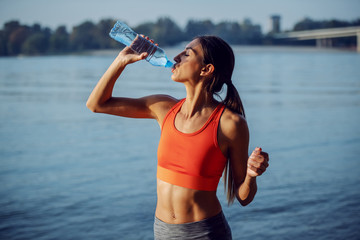 Young attractive fit thirsty sportswoman taking a break after exercising and drinking fresh water....
