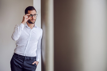 Young geeky thoughtful businessman in shirt leaning on pillar and gazing at something.