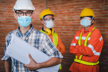 Construction engineers and three architects wear medical masks to prevent coronary infections. Covid-19 - Supervisor and follower wearing masks stand in the construction area.