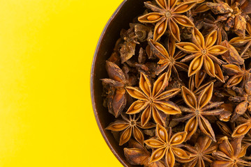 star anise in wooden bowl on yellow background.