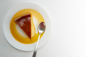 Slice of sugar creamy pudding on white plate with silver spoon.
