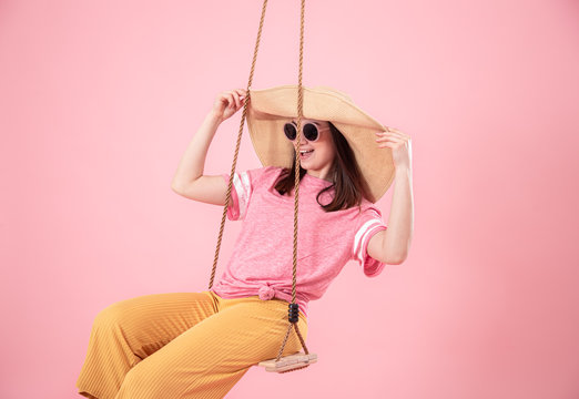 Young woman on a swing on a pink background.