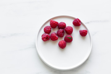 Plate of Fresh Raspberries on white marble background with copy space