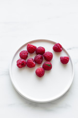 Plate of Fresh Raspberries on white marble background with copy space