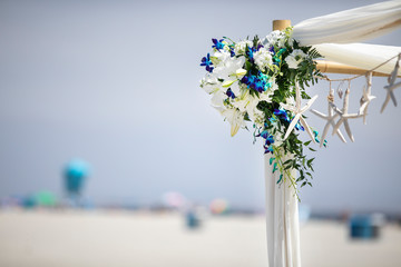 Gazebo decorated with blue and white flowers and white drapes for a wedding party on the beach