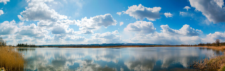 Obraz premium Panoramic landscape from the lake shore with colorful clouds in the spring sun.