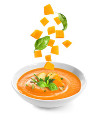 Ingredients falling into bowl of homemade pumpkin soup on white background