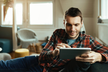 Smiling man surfing the net on touchpad in the living room.