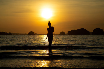 Fototapeta premium Silhouette of a girl on the beach, against the backdrop of the sea and sunset