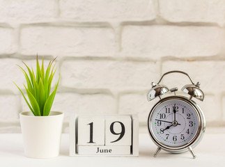 June 19 on a wooden calendar next to the alarm clock on the table. Summer day, empty space for text.Calendar for June on a light background.