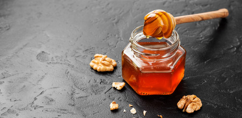 Honey with wooden honey dipper on black table.